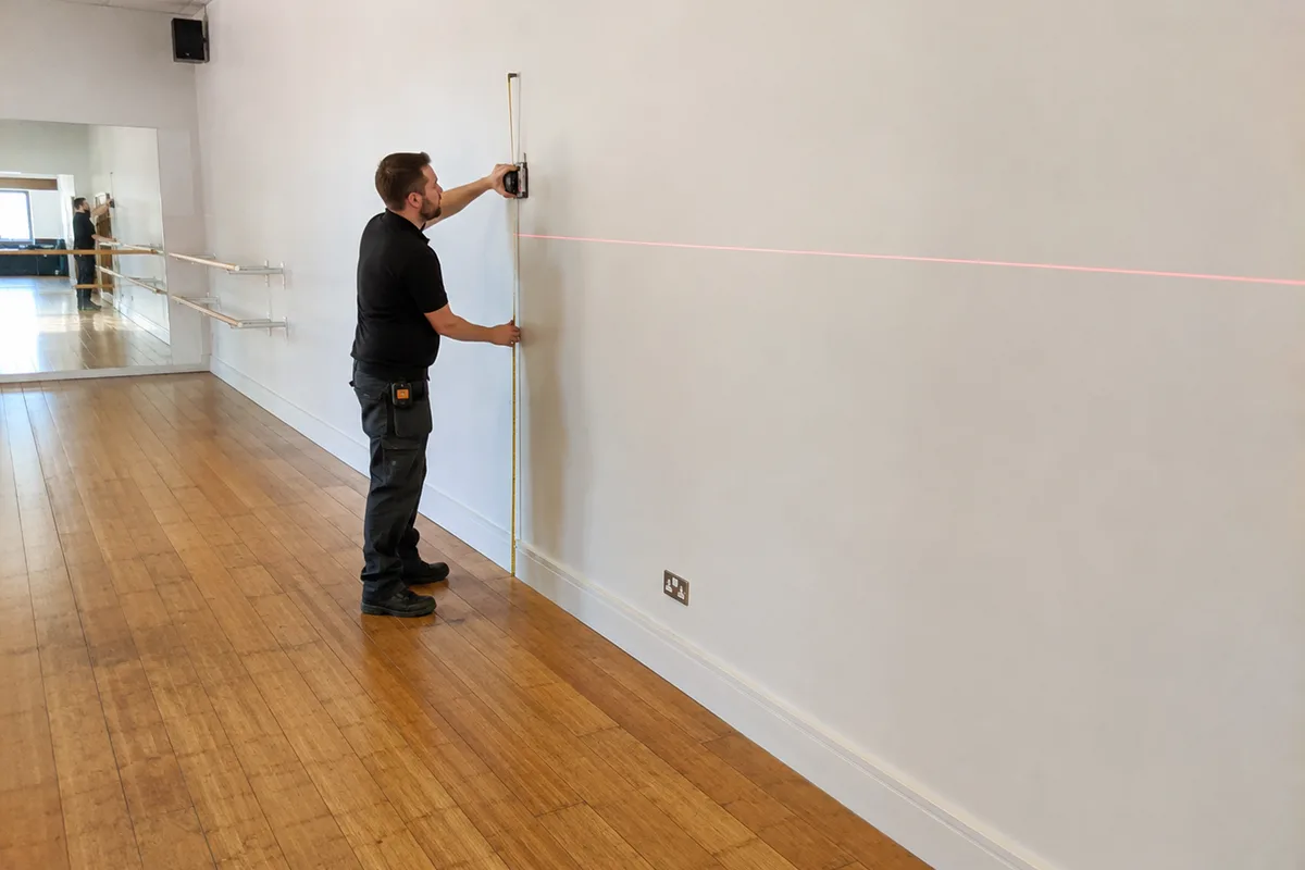 Measuring a dance studio wall for mirror installation with a laser level